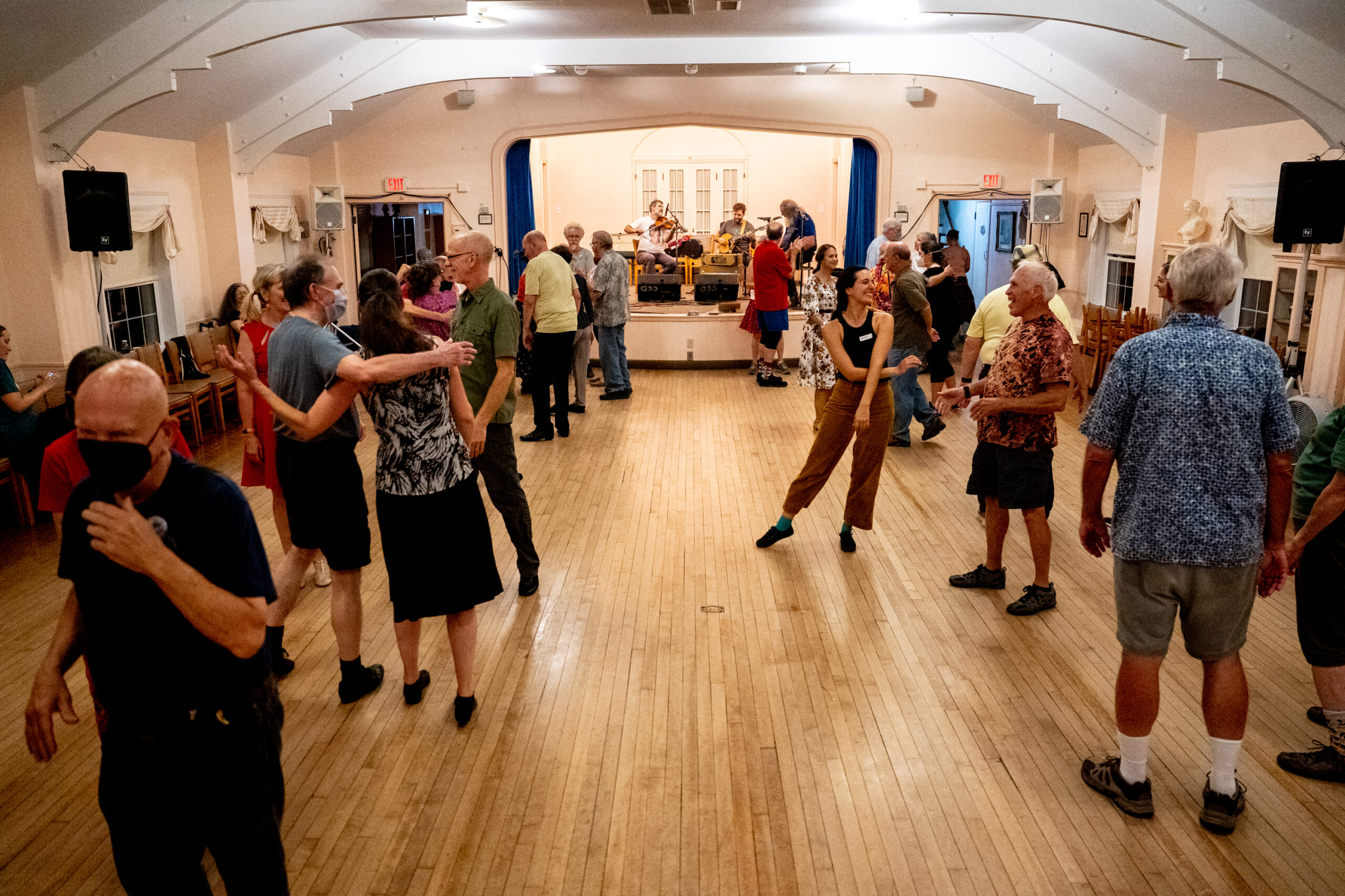 Dozens of people smile and hug each other in a barn-like dance hall.
