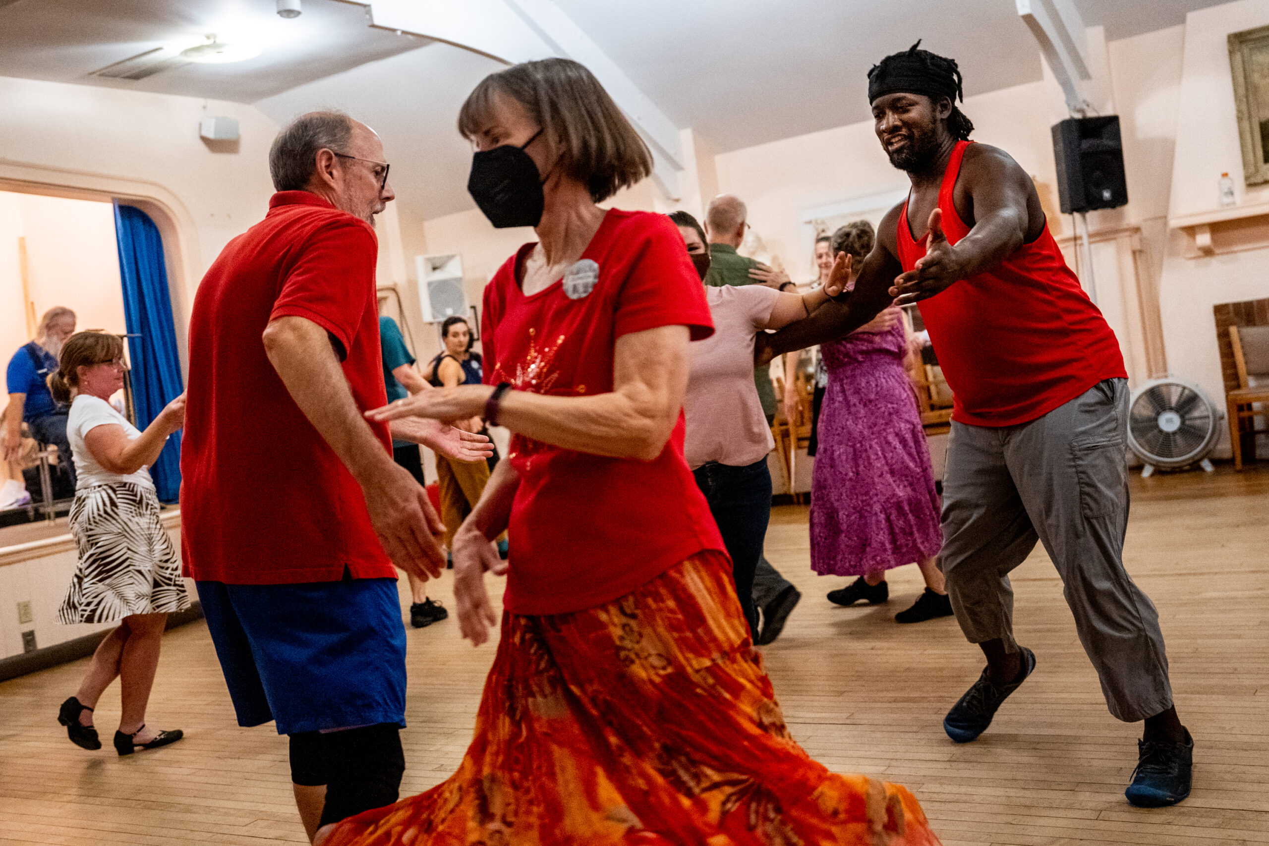 A Black man in his early 40s wearing a red shirt reaches out to a dance partner.