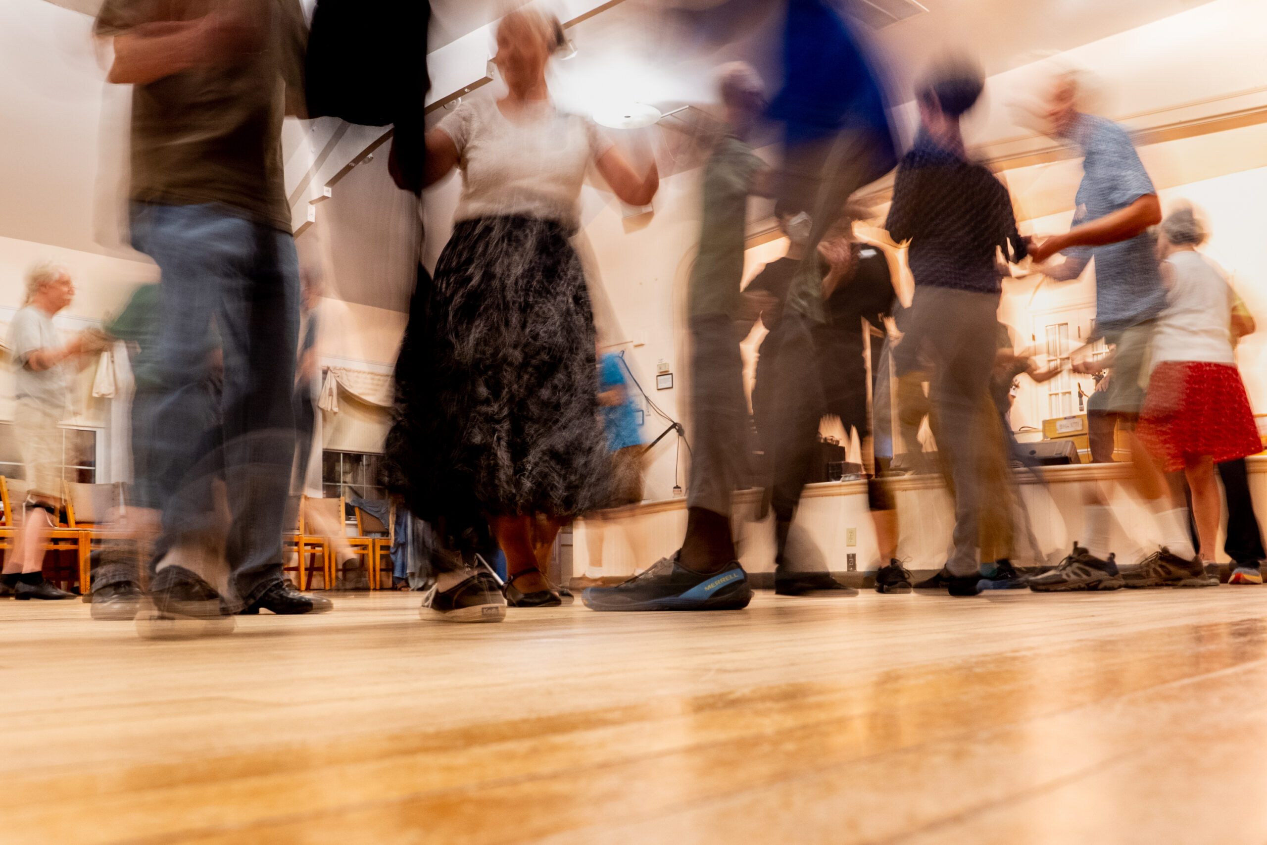 A slow shutter speed shows motion blur of people dancing in a hall.
