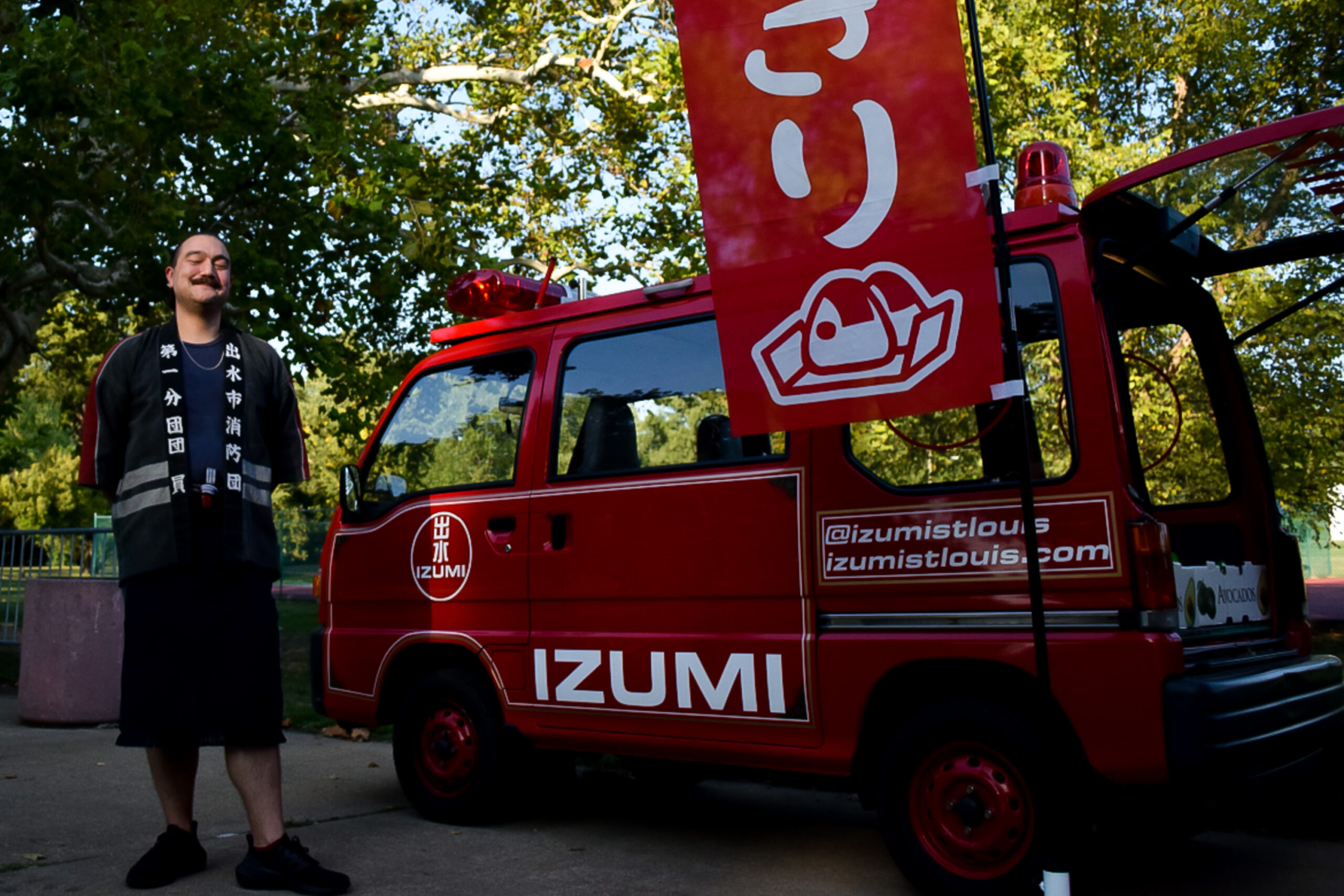 A middle aged fair-skinned man stands next to a Japanese fire truck in a park.